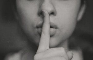 Black and white image of a finger held up to a pair of pursed lips, making the 